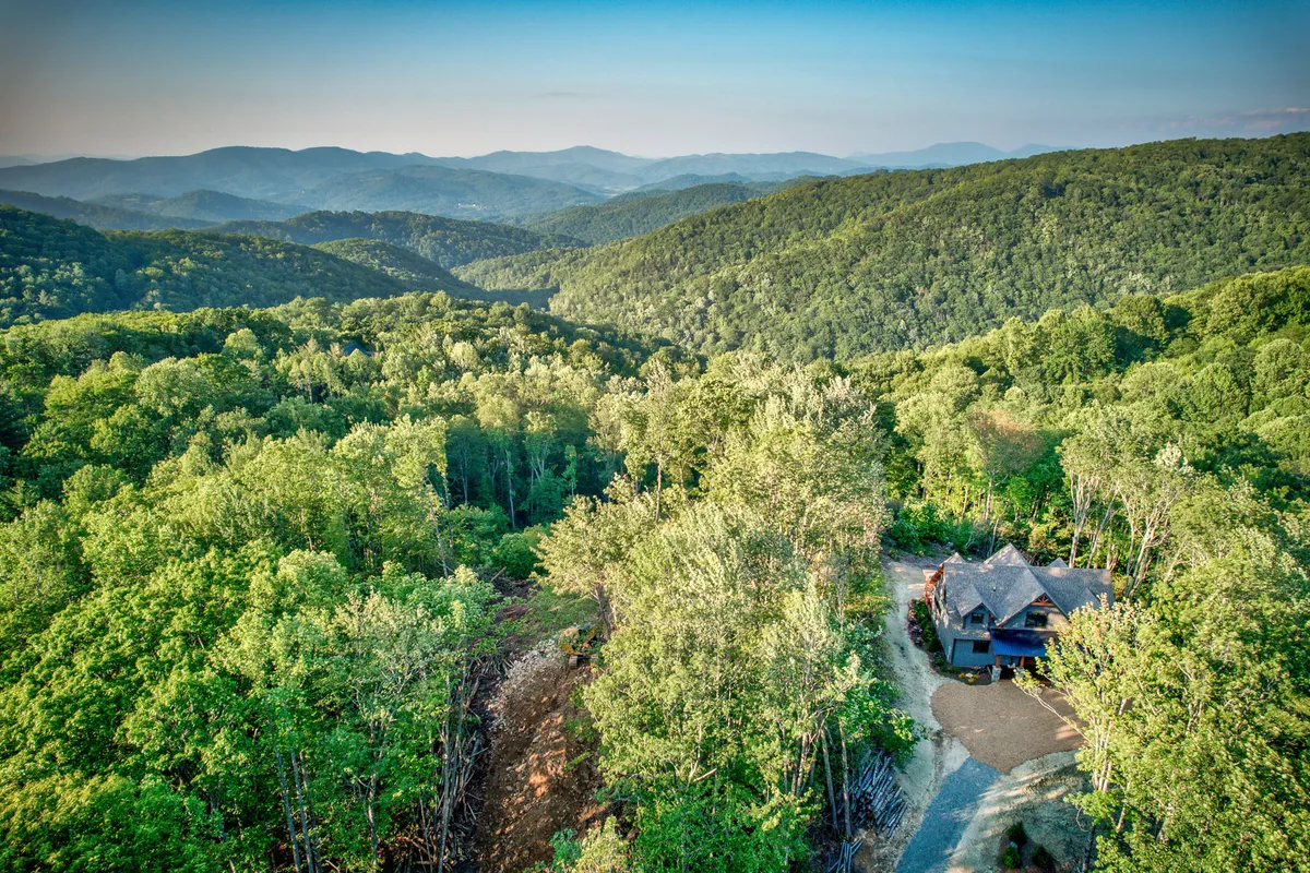 A picturesque exterior view of the mountain home, surrounded by lush trees and with a sweeping mountain range in the background. The scene evokes tranquility and a strong connection to nature, while the house appears inviting and spacious—a fitting base for family adventures.
