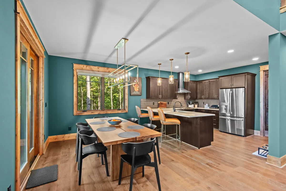 This scene features a dining table set near large windows for enjoying views while dining, with a kitchen island nearby for casual conversations and meal prep. Stylish lighting fixtures and a warm palette create an inviting, social setting for both meals and gatherings.
