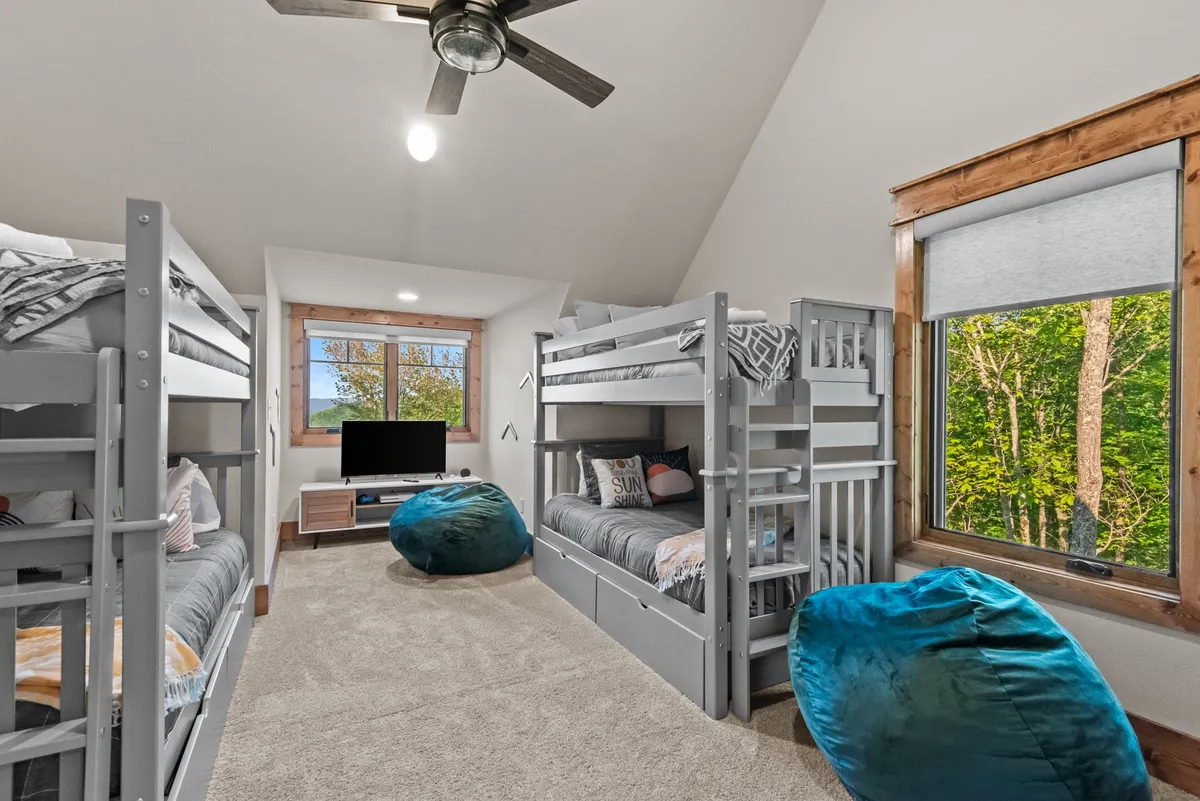 A playful bunk room with multiple bunk beds, bean bag chairs for lounging, a TV unit, and a large window with scenic views. The space is designed for fun, featuring elements perfect for younger guests, such as an Xbox console and cozy spots to play or relax.