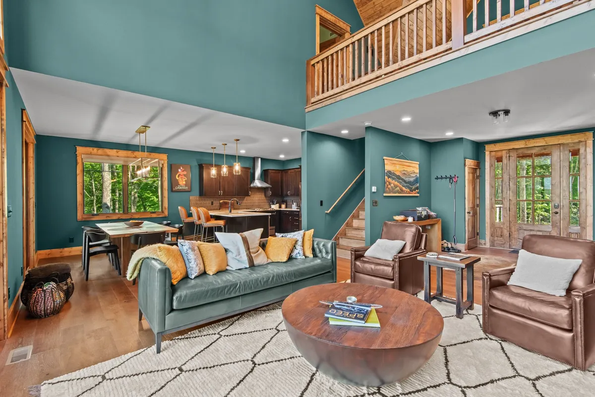 A bright, modern interior with green accent walls, expansive windows, a wooden staircase, and a dining area. Though not explicitly showing pet items, the space feels open, welcoming, and suitable for a pet-friendly home setup.