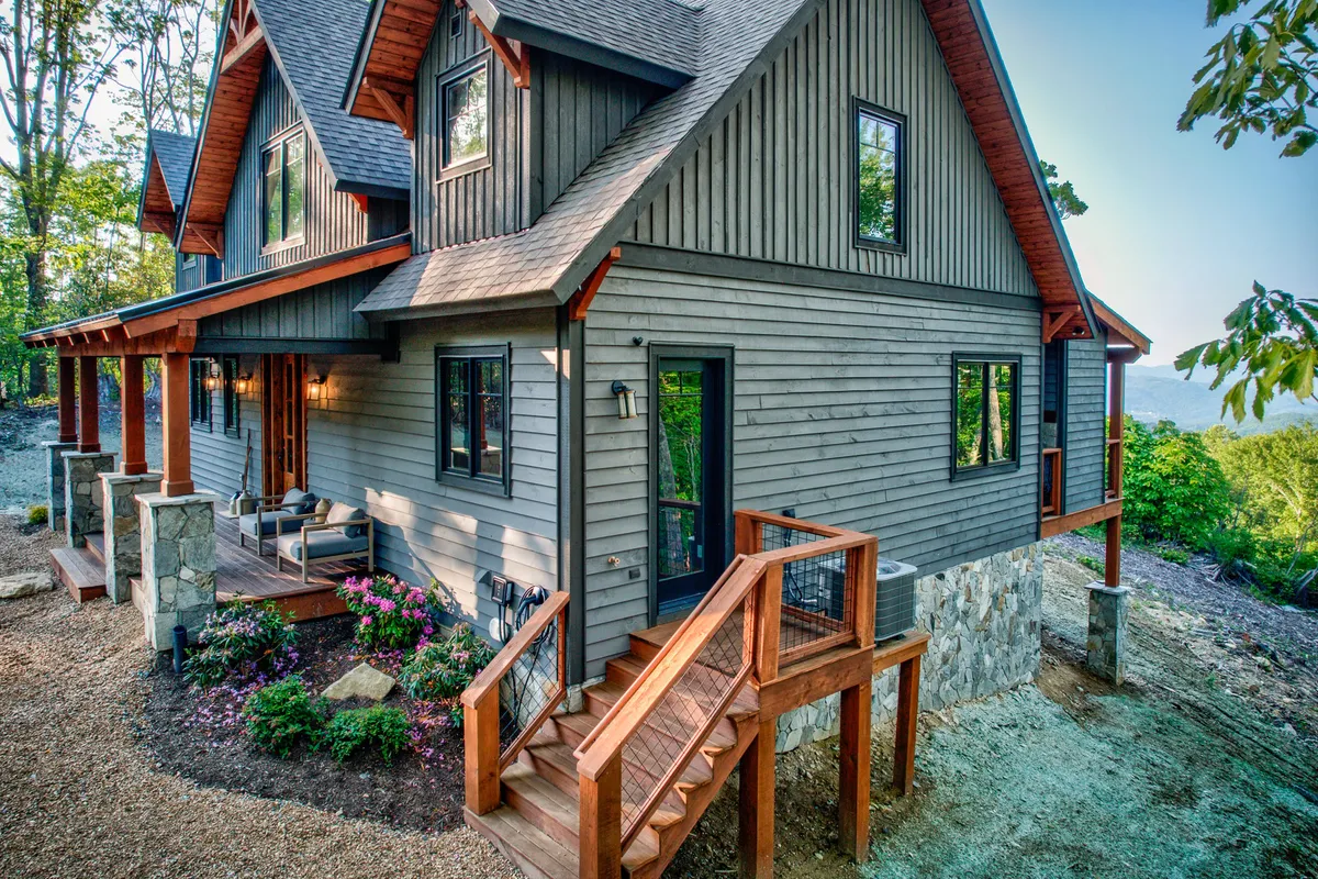 An exterior view of wooden stairs and a stone-based home with colorful flower gardens and large windows. The surrounding area hints at access to nature trails and a welcoming, dog-friendly environment.