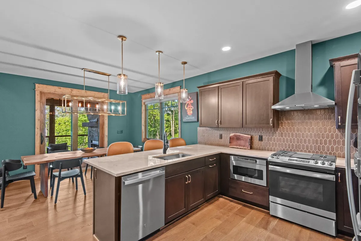This image showcases a spacious kitchen island and adjacent dining table, with large windows bringing in abundant natural light and offering scenic views. The open plan allows for easy interaction between the kitchen and dining spaces, reflecting a social, communal atmosphere ideal for group meals and conversations.